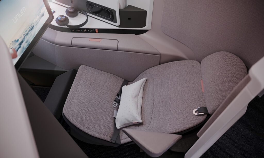 Aerial view of the Unum One seat. A pillow rests on a grey business class seat. Headphones rest on a side table next to an IFE screen.