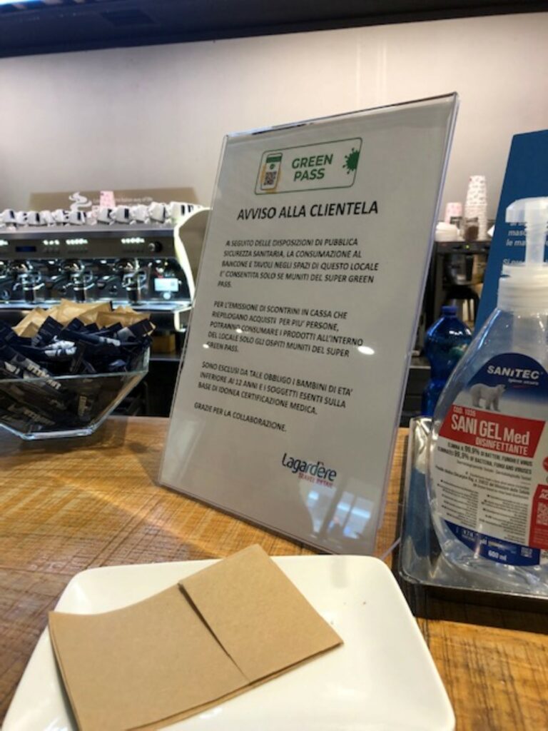 A sign showing that a "green pass" is required to enter is sitting on a table next to a bottle of hand sanitizer