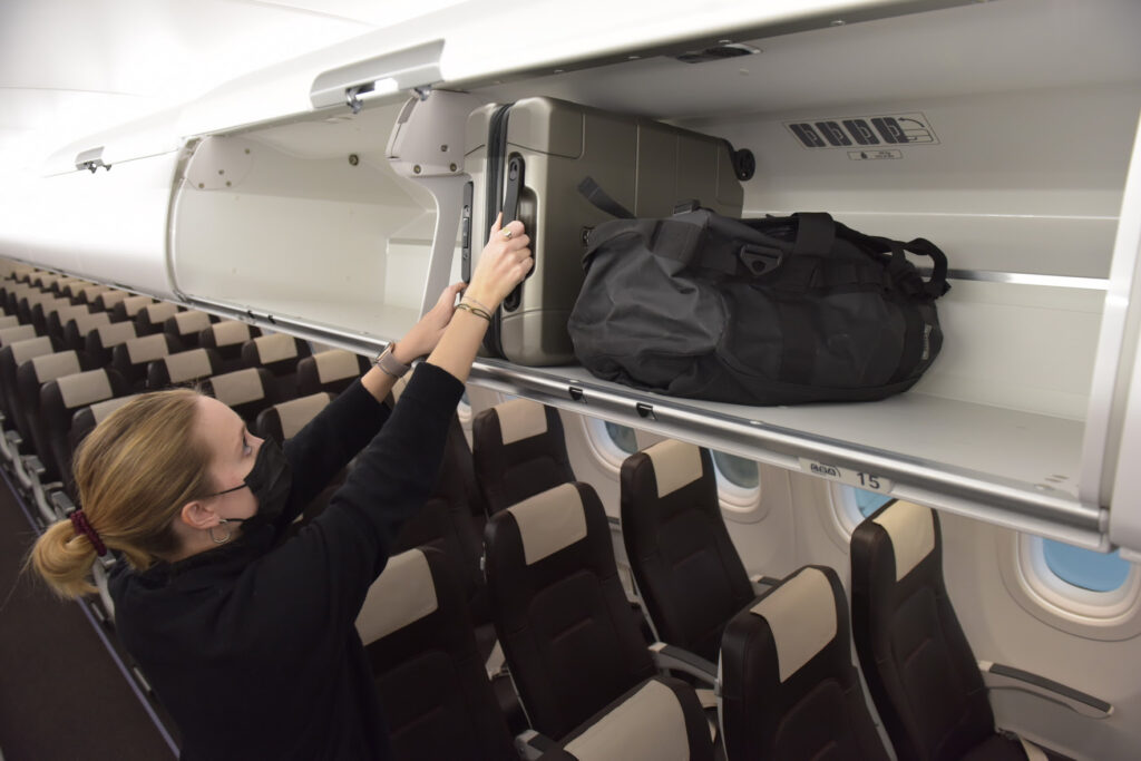 SWISS Airbus Airspace Cabin. A masked flight attendant is placing luggage in the overhead bin