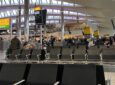 Heathrow Airport is busy with passengers in the distance but many empty seats remain in the forefront of the image.
