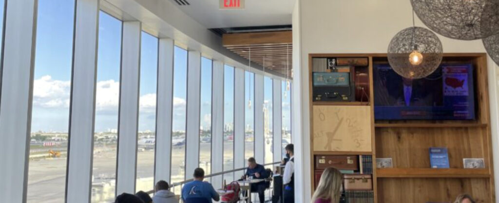 Inside the Amex lounge with ground to ceiling windows allowing lots of lots in, and passengers seated, eating and working