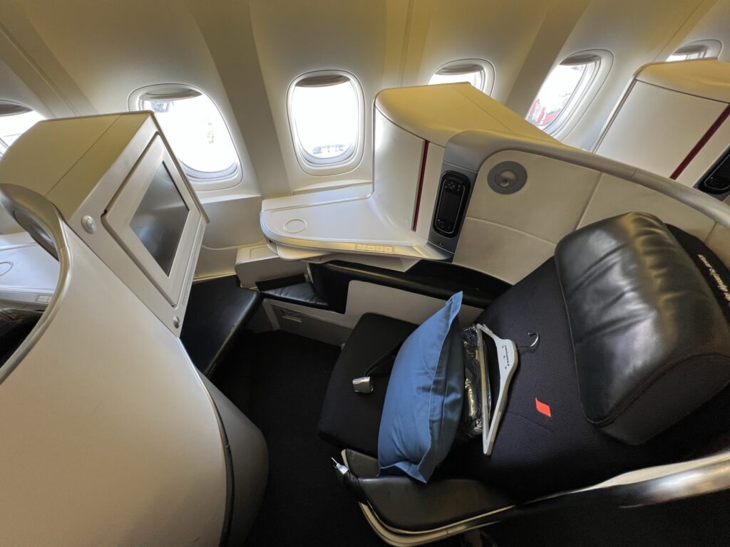 Air France Boeing 777-300ER business class seat. The seat has a pillow, blanket and hanger sitting on it. The seat is dark blue with grey thermoplastics wrapping around it.