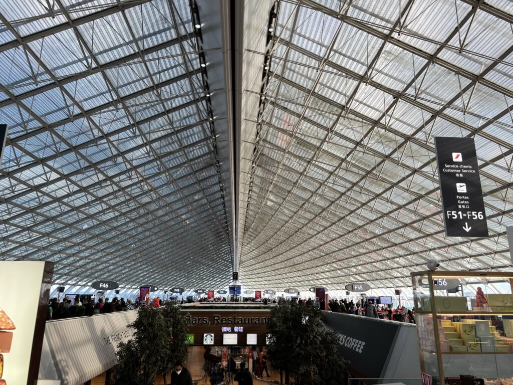 A crowded airport is pictured here. The airport has high ceilings made of all windows.