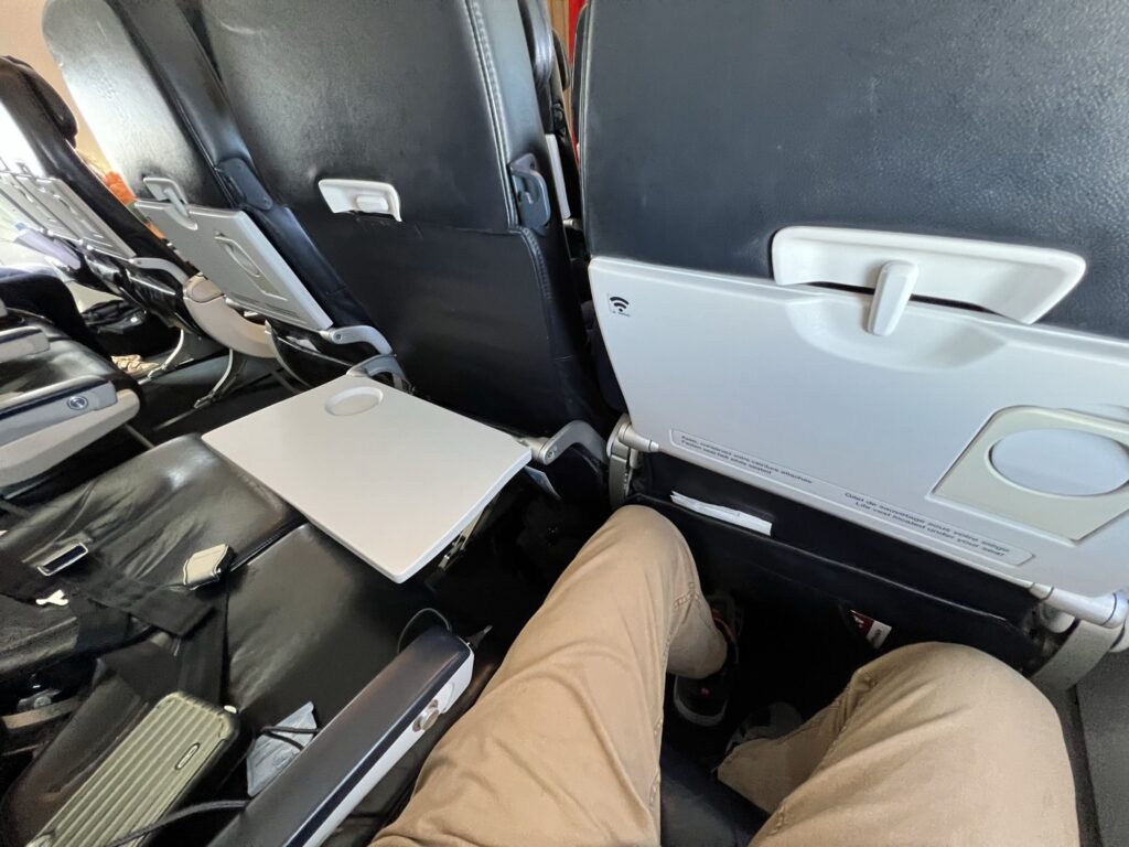 The knees of a man are seen here while sitting in an aircraft seat. The seat next to the man is blocked off. 