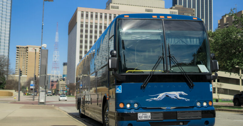 Greyhound bus is driving down the road of a city.
