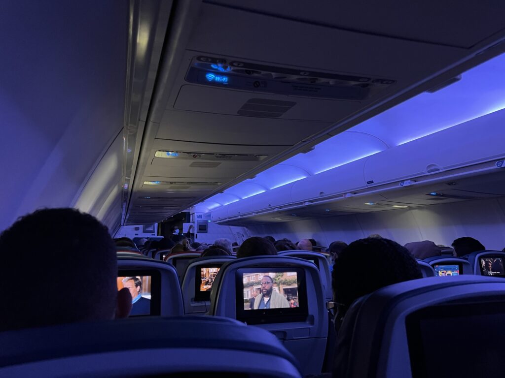 Delta 757-200 cabin interior with blue LED lighting. The view is from the back of the aircraft and shows the IFE screens at each seat.