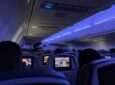 Delta 757-200 cabin interior with blue LED lighting. Passengers are throughout the aircraft. The view is from the back of the aircraft showing the IFE screens at each seat.