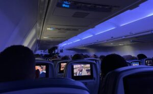 Delta 757-200 cabin interior with blue LED lighting. Passengers are throughout the aircraft. The view is from the back of the aircraft showing the IFE screens at each seat.