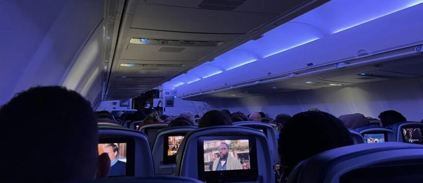 Delta 757-200 cabin interior with blue LED lighting. Passengers are throughout the aircraft. The view is from the back of the aircraft showing the IFE screens at each seat.