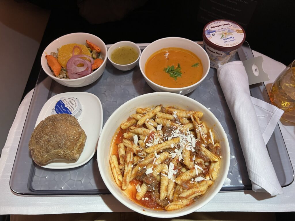 A meal is displayed on the tray table of the Delta One suite. There is soup, bread and a main entrée. 