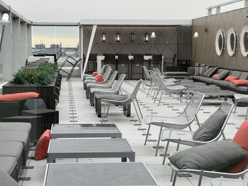 The outdoor terrace in the SkyClub at JFK T4 is filled with empty chairs and tables. Orange pillows create pops of color throughout the terrace. 