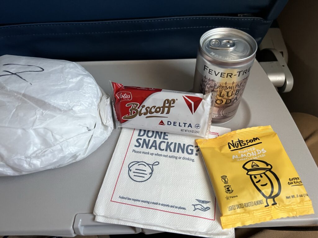 A mini can of soda and a couple of small packaged snacks sit on a tray table.