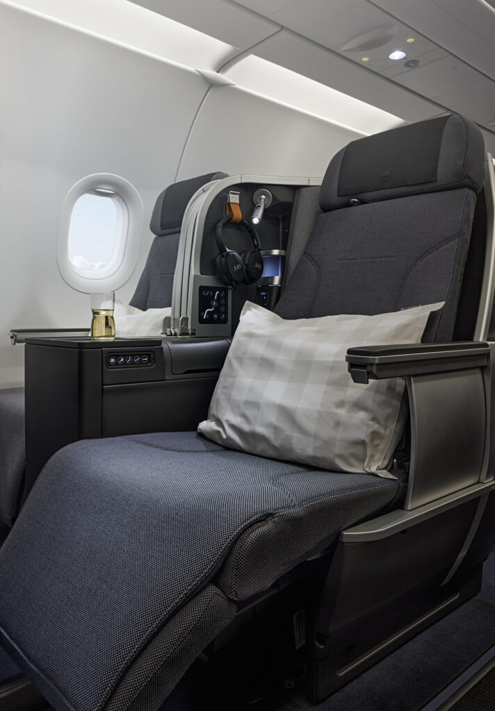 SAS Thompson Vantage seat is pictured here in various grey tones. Headphones ang to the side of the seat and a white a grey plaid pillow sits on top of the seat.