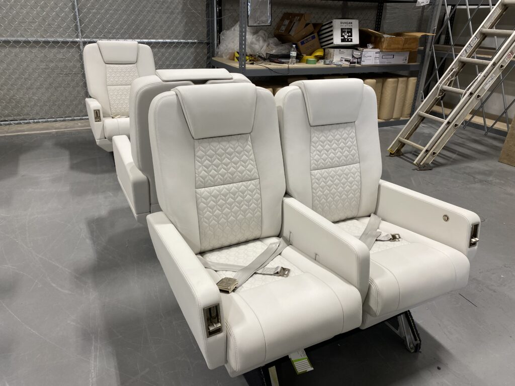 A set of two all white leather business aviation aircraft seats sit on the Latitude Aero factory floor. 