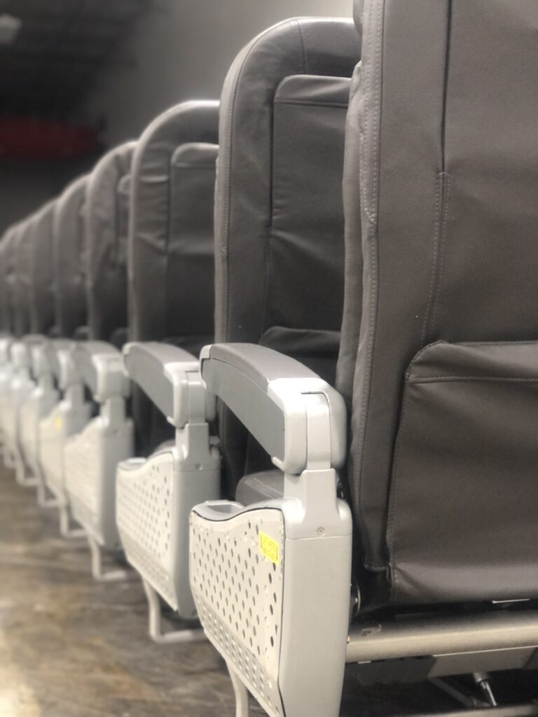 Close up view of a row of grey aircraft seats on the factory floor. This view is from the back of the seats. 