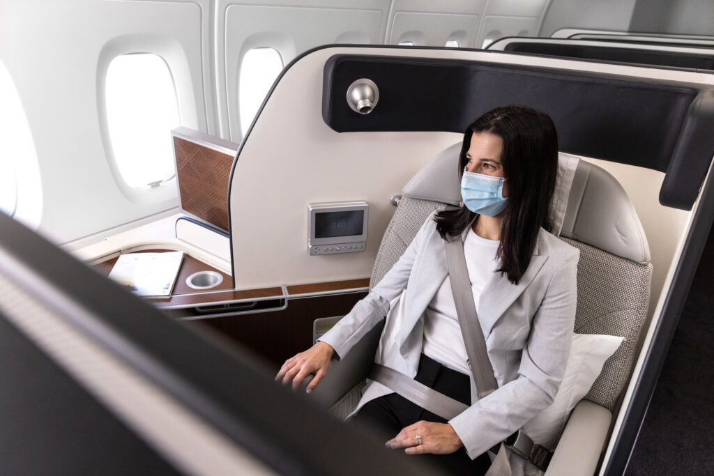 A female passenger is masked while sitting in Qantas First Class seat. She is wearing the 3-point seatbelt.