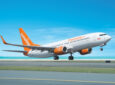 Sunwing aircraft is taking off. The sky is crystal clear blue. The aircraft is all white with an orange tail, engines and wingtips.