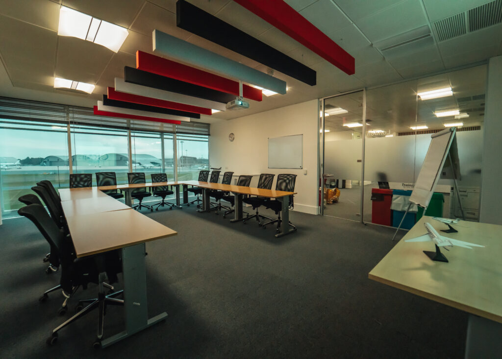 TAG Training facility has floor to ceiling windows. A large u-shapped table is in the center of the room with grey chairs set up around the outside of it.