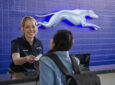 Greyhound employee is handing a passenger their ticket to board the bus.