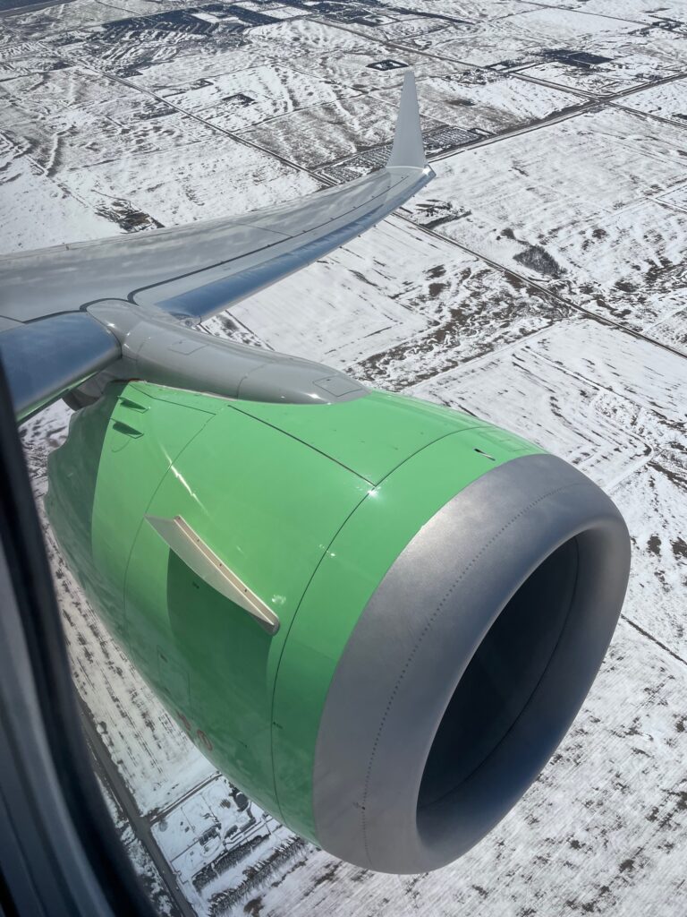 A view of Flair Airlines wing and green engine over the snowy landscape of the Canadian West Coast.