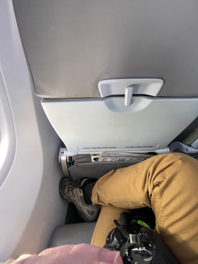 A mans knees are show the tight space in between seats on Flair Airlines Boeing 737 MAX 8