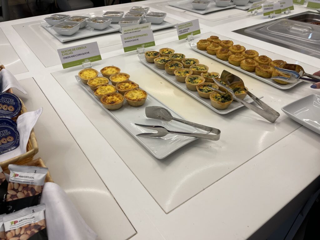 Rows of various types of quiche are laid out on white tableware in the TAP lounge.