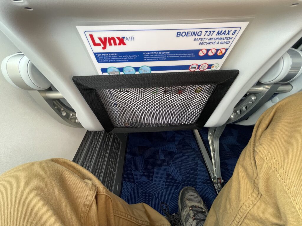 A man's knees are pictured here along with the seatback of the aircraft seat in front of him.