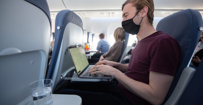 A man is working on his laptop on the aircraft tray table.