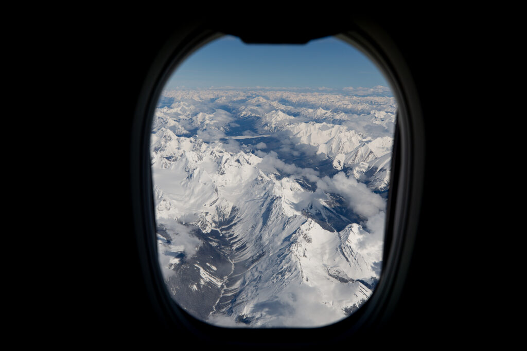 Looking out an aircraft window over snowy mountain tops.