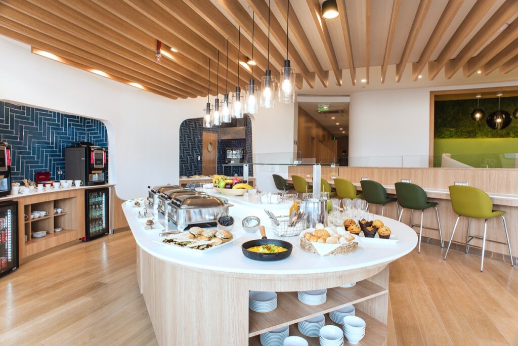 Brightly lit SkyTeam lounge in Santiago. The buffet is centered in the lounge with high tables to the side of it.