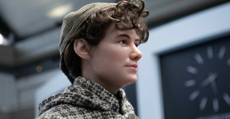 Nellie Bly statue close up. She is wearing a plaid overcoat and a small brown hat.