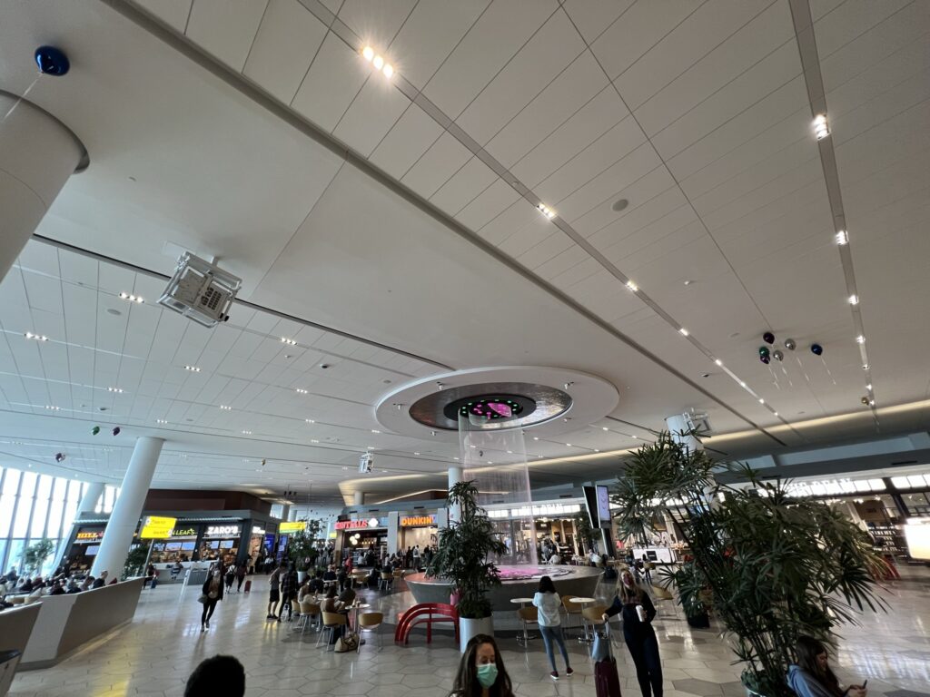 LaGuardia Airport Terminal B is busy with activity and people. A large waterfall fountain is in the center of the terminal. 