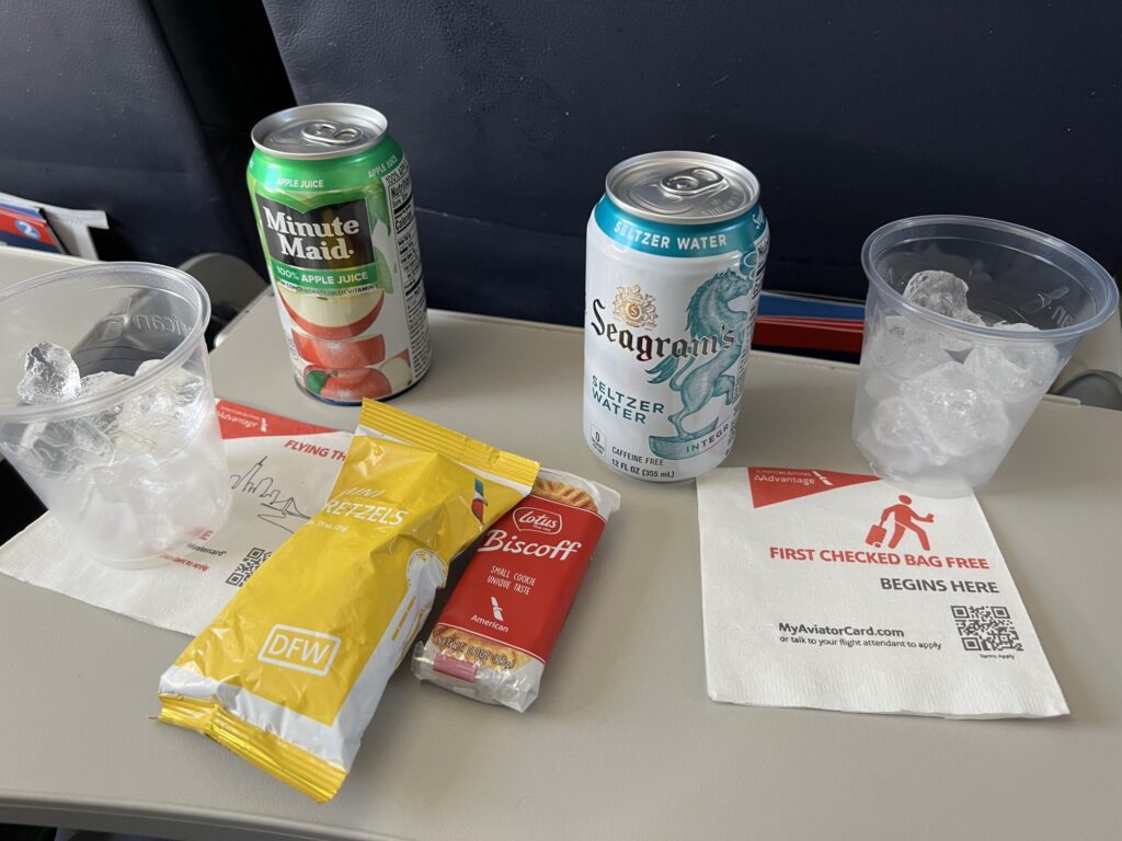 A variety of drinks and and snacks are displayed on the American Airlines' aircraft tray table for an American Eagle flight.