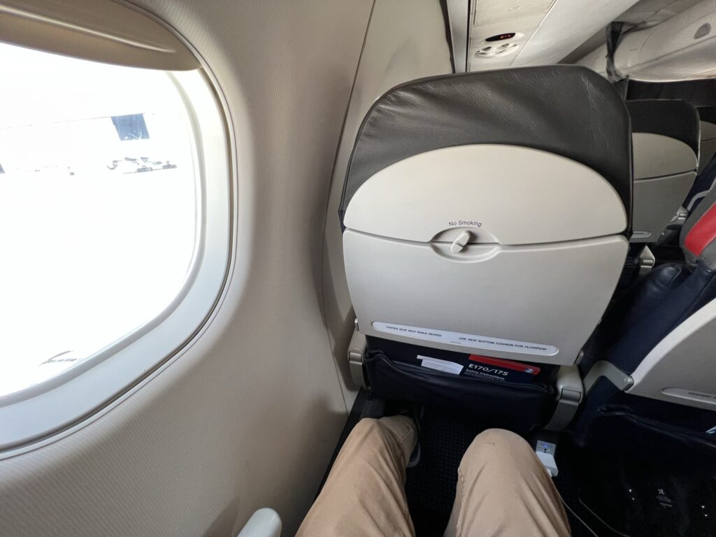 A man's knees are visibly close to the American Airlines' aircraft seat in front of him.