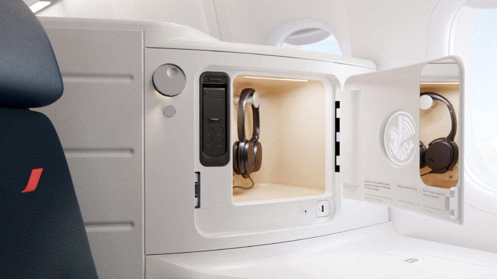 A cubby in Air France's Business Class seat is all white with a pair of headphones hanging in it and a remote embedded in the wall beside it.