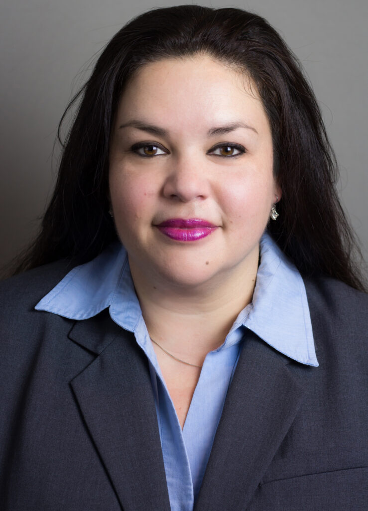 Headshot of Corinne Streichert in a grey business suit with blue shirt