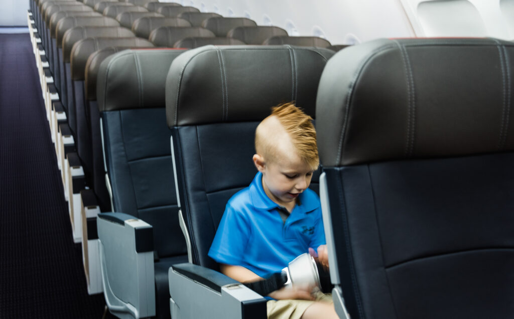 A young boy sits alone in an empty aircraft cabin playing with his seatbelt.