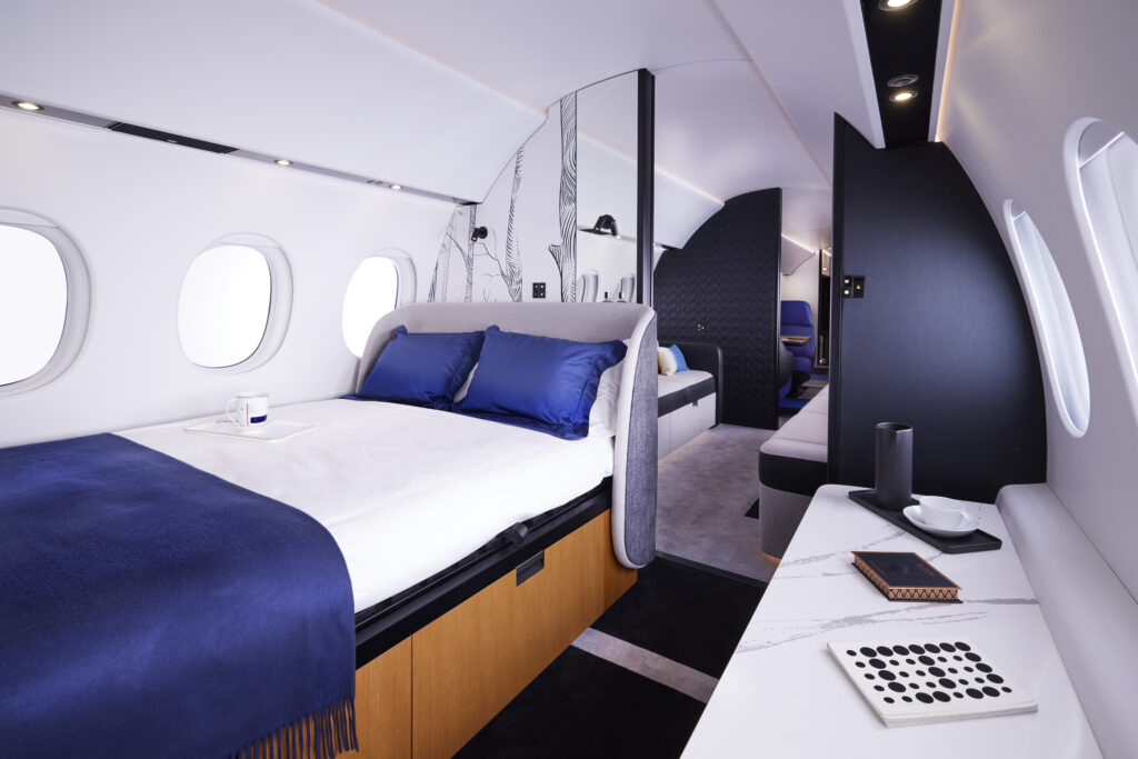 Dassault Falcon 10X interior showing a comfortable looking bed with blue and white linens.