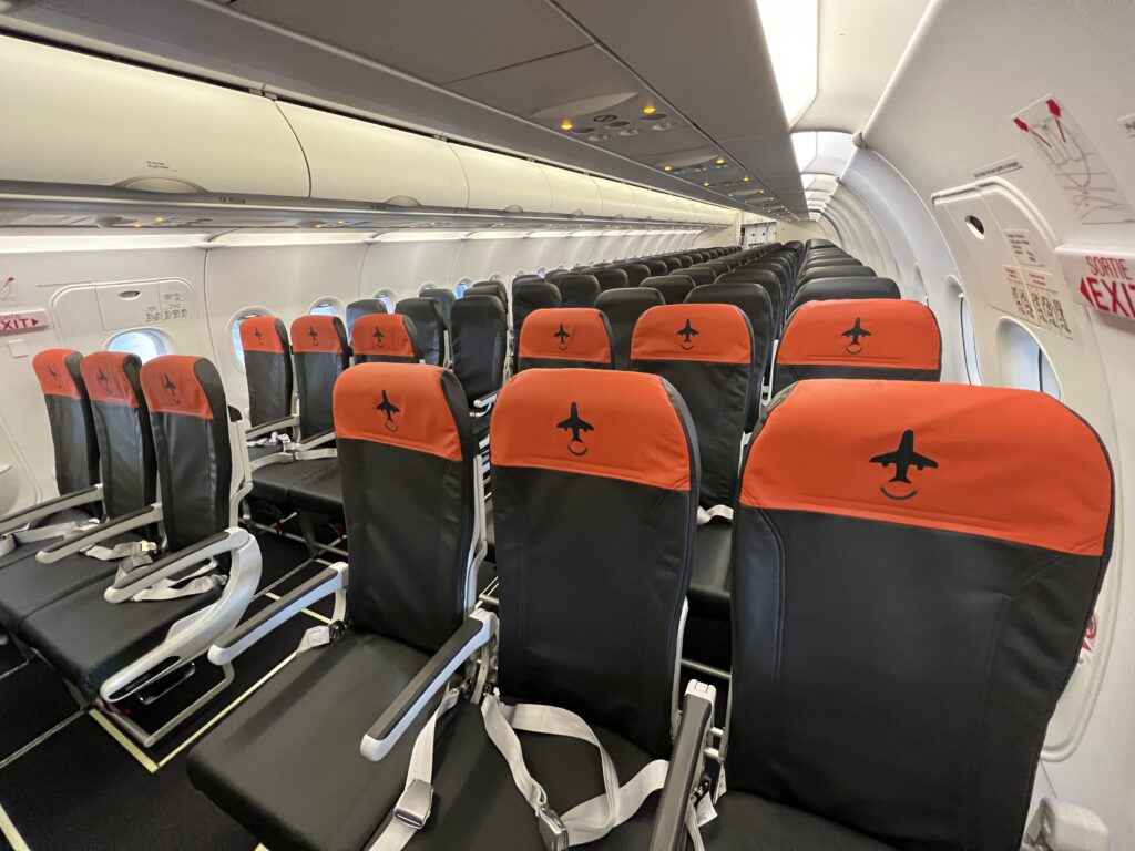 Canada Jetlines A320 cabin interior. The seats are grey, with some seats having orange headrests. The seats are arranged in a 3-3 configuration.