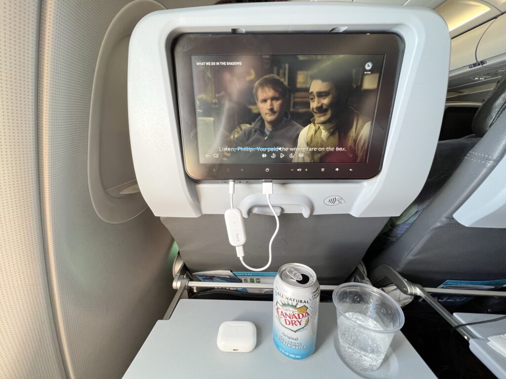 A show is playing on the seatback IFE, with light streaming in from the window. 