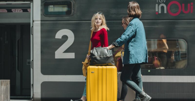 A group of 3 people are standing with their luggage in front of a train entrance.