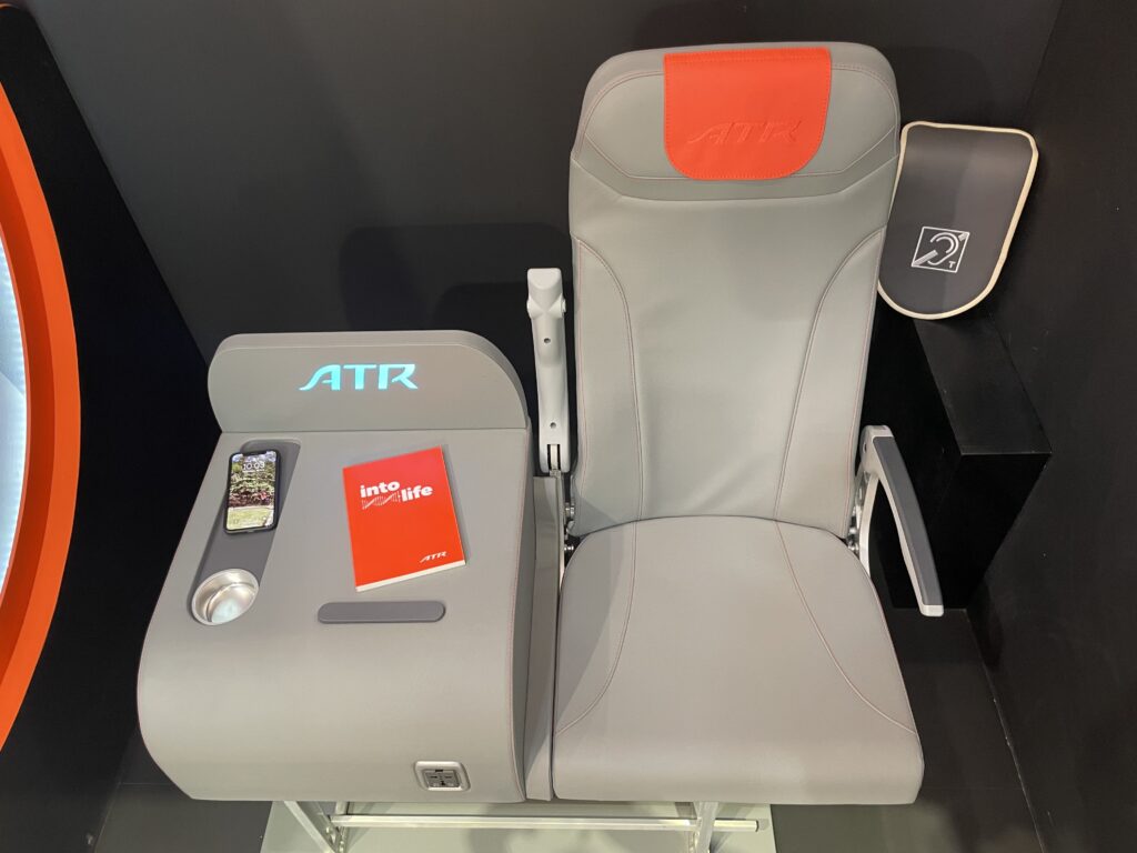 A grey ATR aircraft seat and side table are displayed with Orange accents at the AIX 2022 show floor.