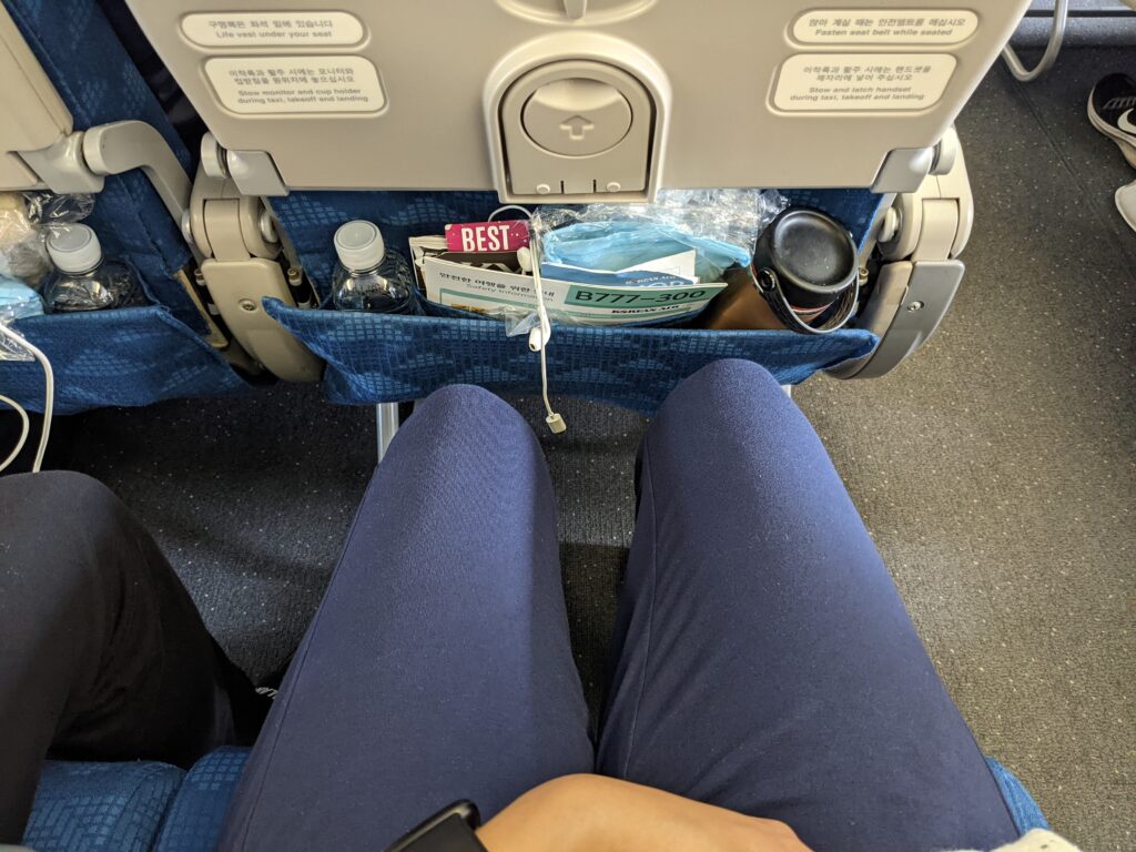 Korean Air 777-300 ER Excellent economy class legroom. The image shows a man's knees and the seatback in front of him.