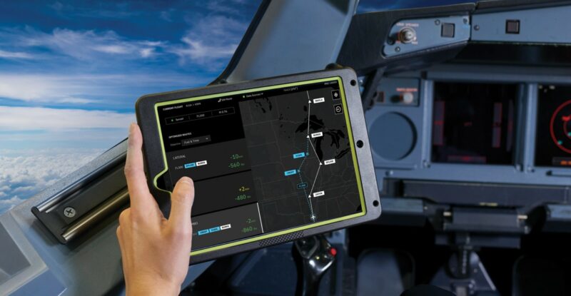 A hand is holding up a tablet with navigational information on it in the cockpit of an aircraft.