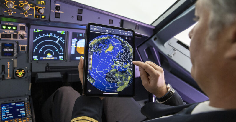 A pilot is looking at his navigation tablet in the cockpit of an aircraft.