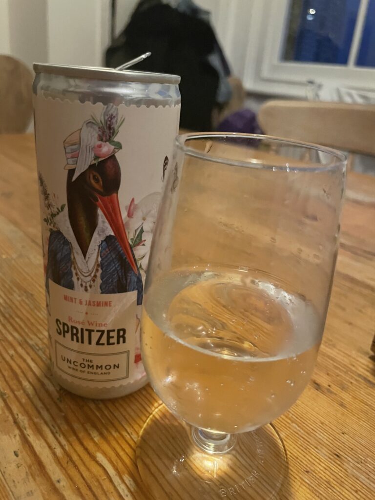 A can of spritzer is sitting on the table next to a glass that is filled with it.