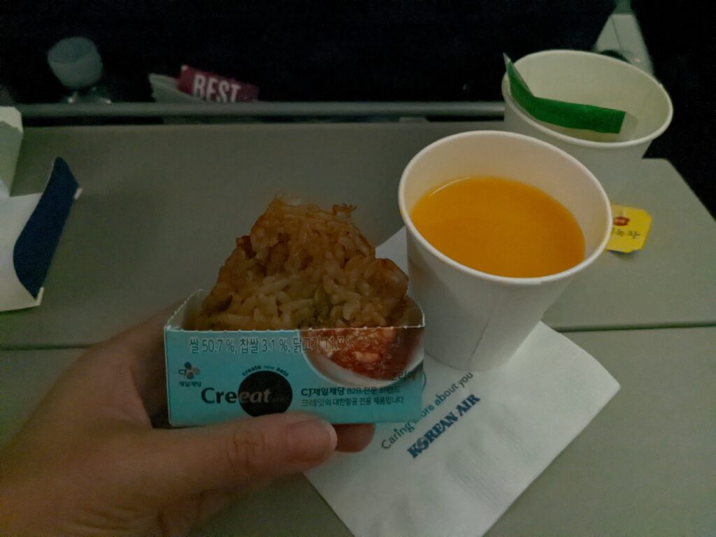 Rice ball snack and a cup of juice are sitting on the aircraft tray table