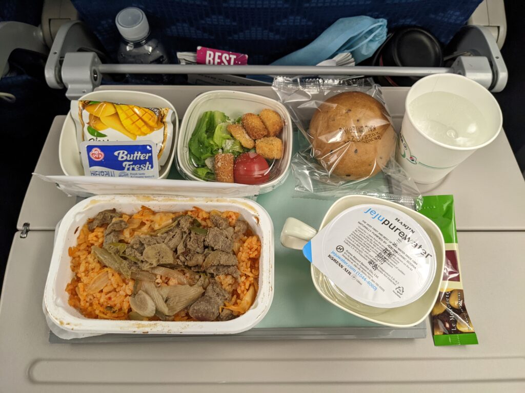 A full mean with entrée, vegetables, bun, dessert and drink are displayed on an aircraft table.