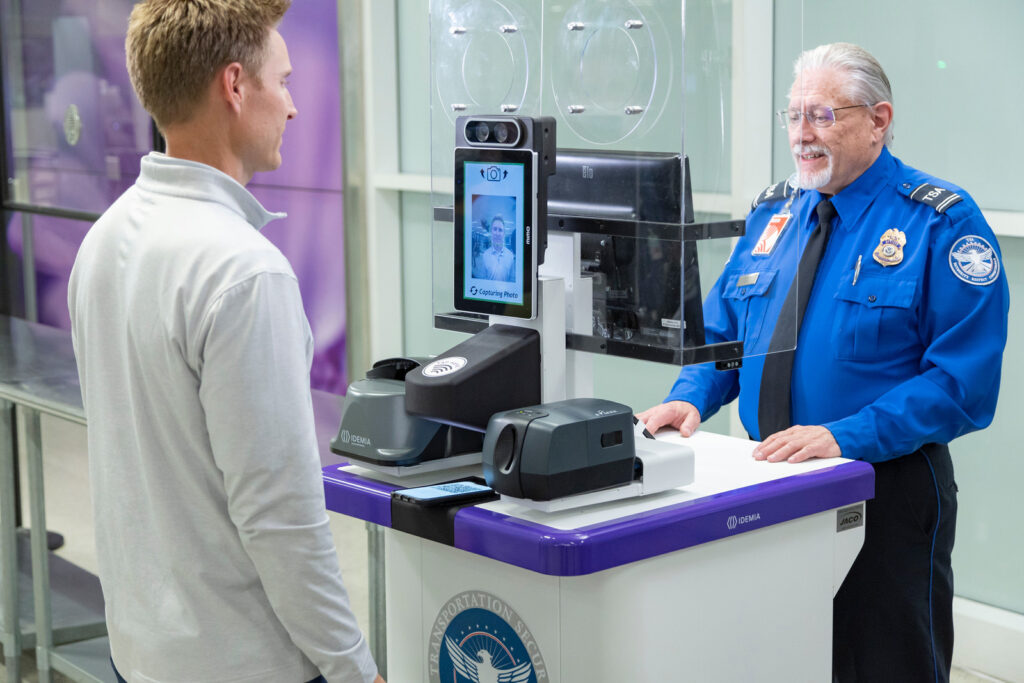 A male TSA agent is checking the ID of A male passenger via facial recognition.