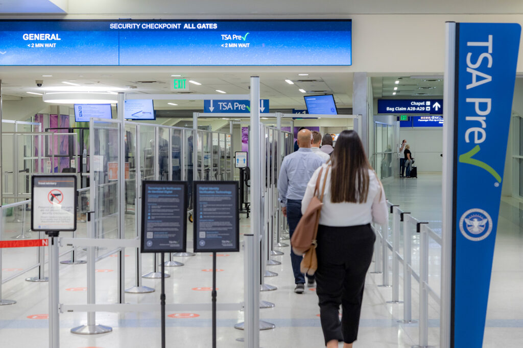 A man and woman are walking into the security area at an airport.